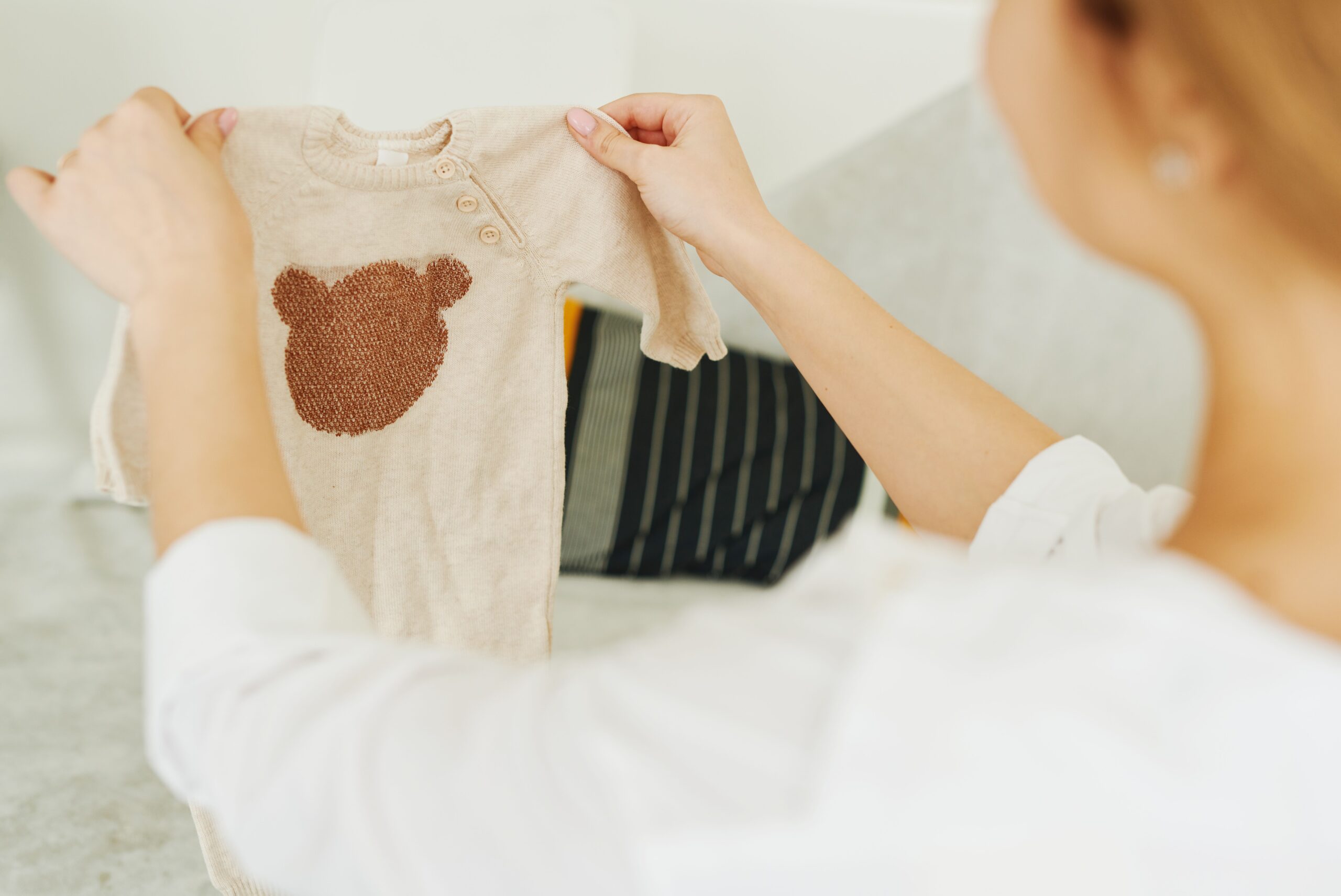Lachende, gl&uuml;ckliche Mutter nutzt den Produktfinder beim Auspacken von Babykleidung
