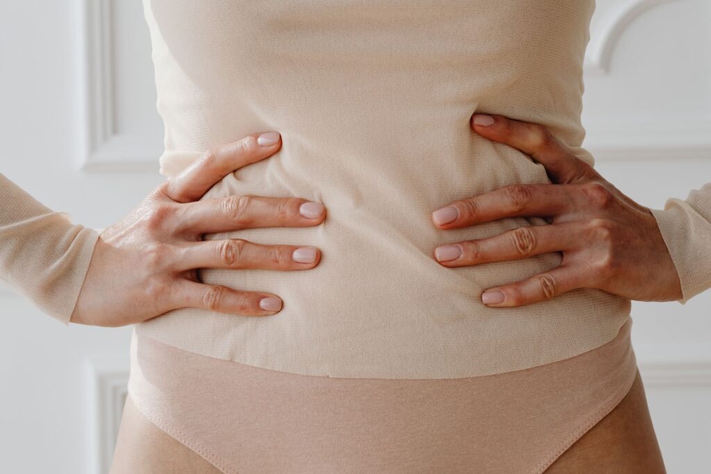 Frau legt die Hände an die Taille: sanfte Stütze für Bauch und Rücken nach der Geburt